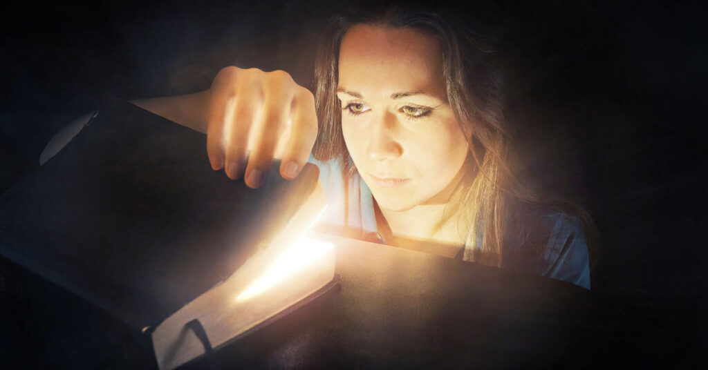 Woman looking into a glowing Bible - Should I read the Bible? What Christians Should Know