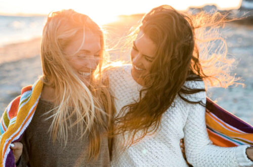 Two young women laughing wrapped in a blanket on the beach